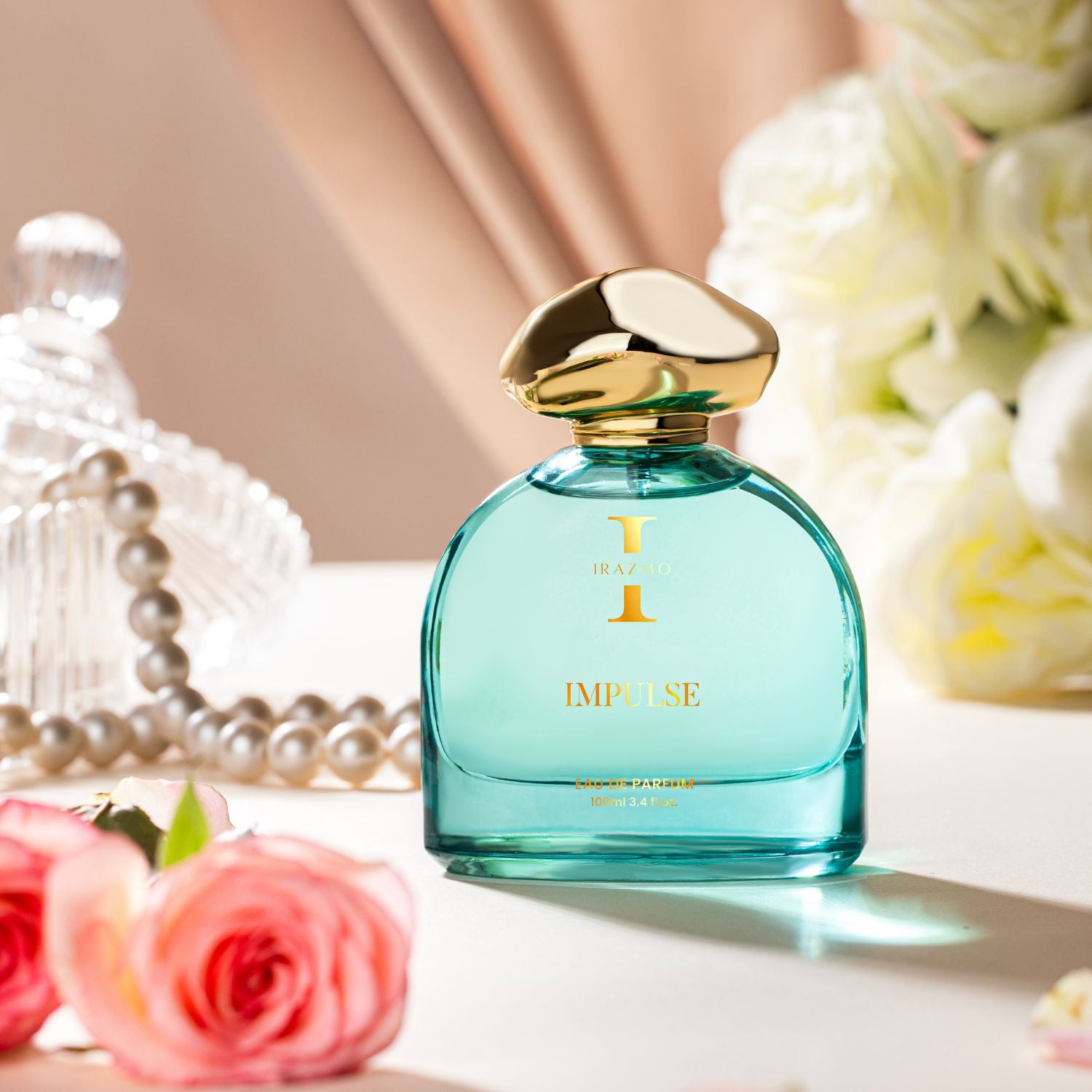 Blue perfume bottle with gold cap on a table with flowers and jewelry in the background