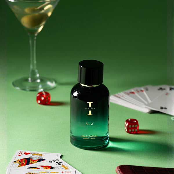 Perfume bottle labeled 'Slay' on a green table with playing cards and dice.