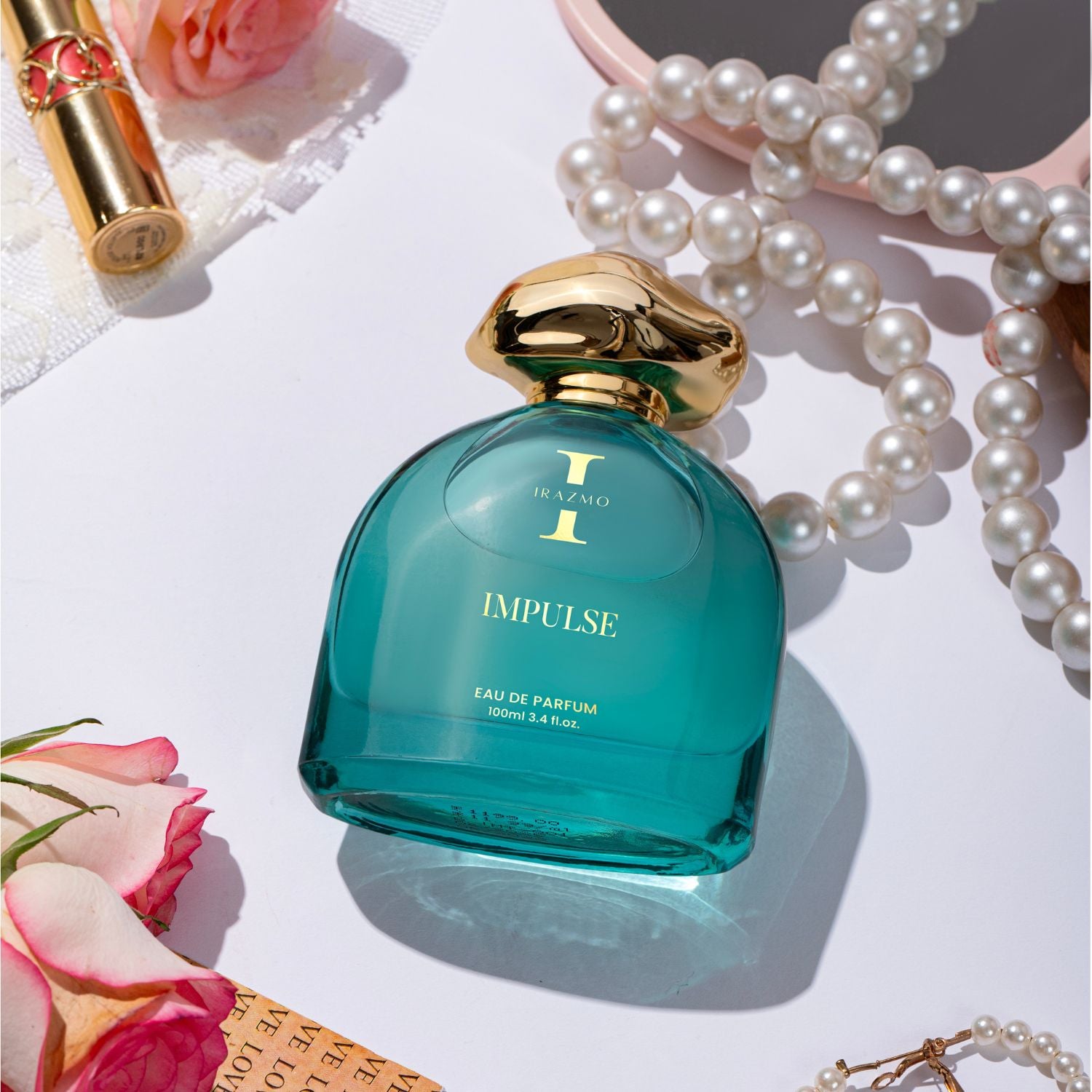 Teal perfume bottle with gold cap on a white surface with pearls and roses.