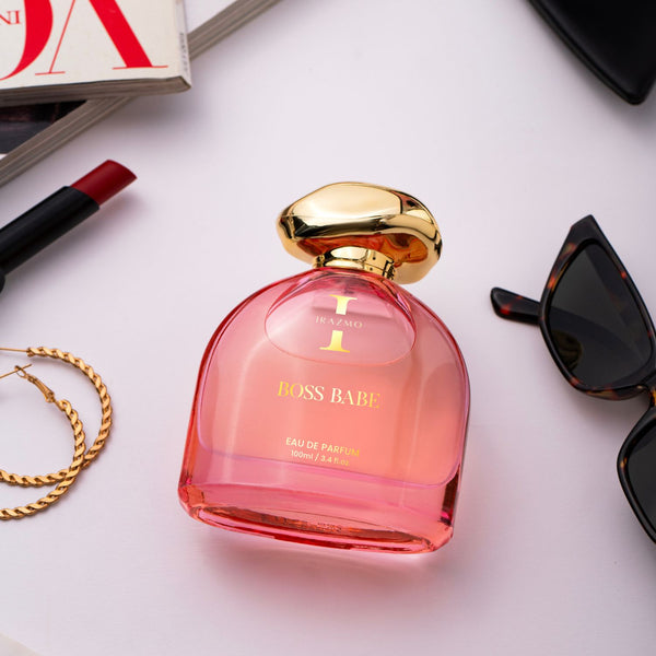 Pink perfume bottle with gold cap on a white surface with accessories.