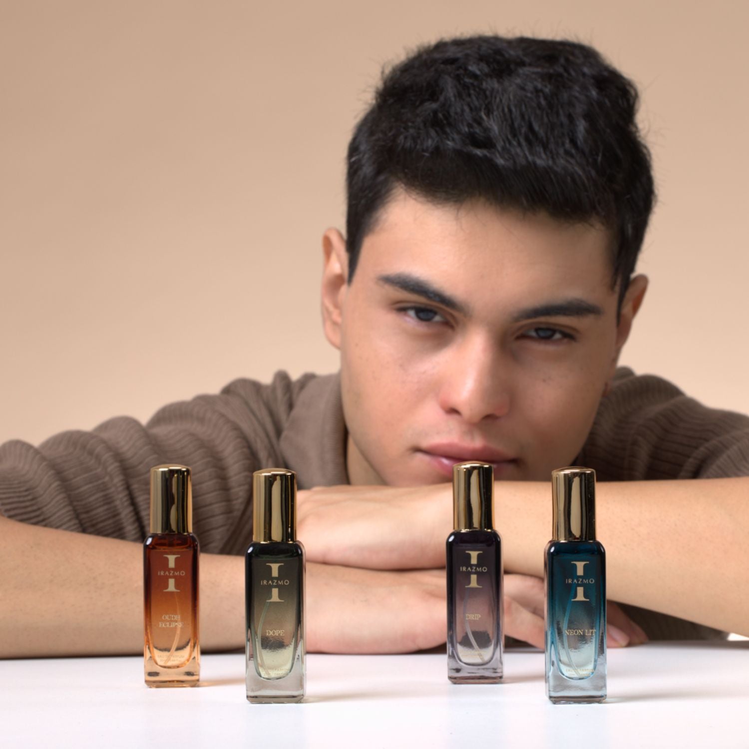 Man leaning on a surface with four perfume bottles in front of him