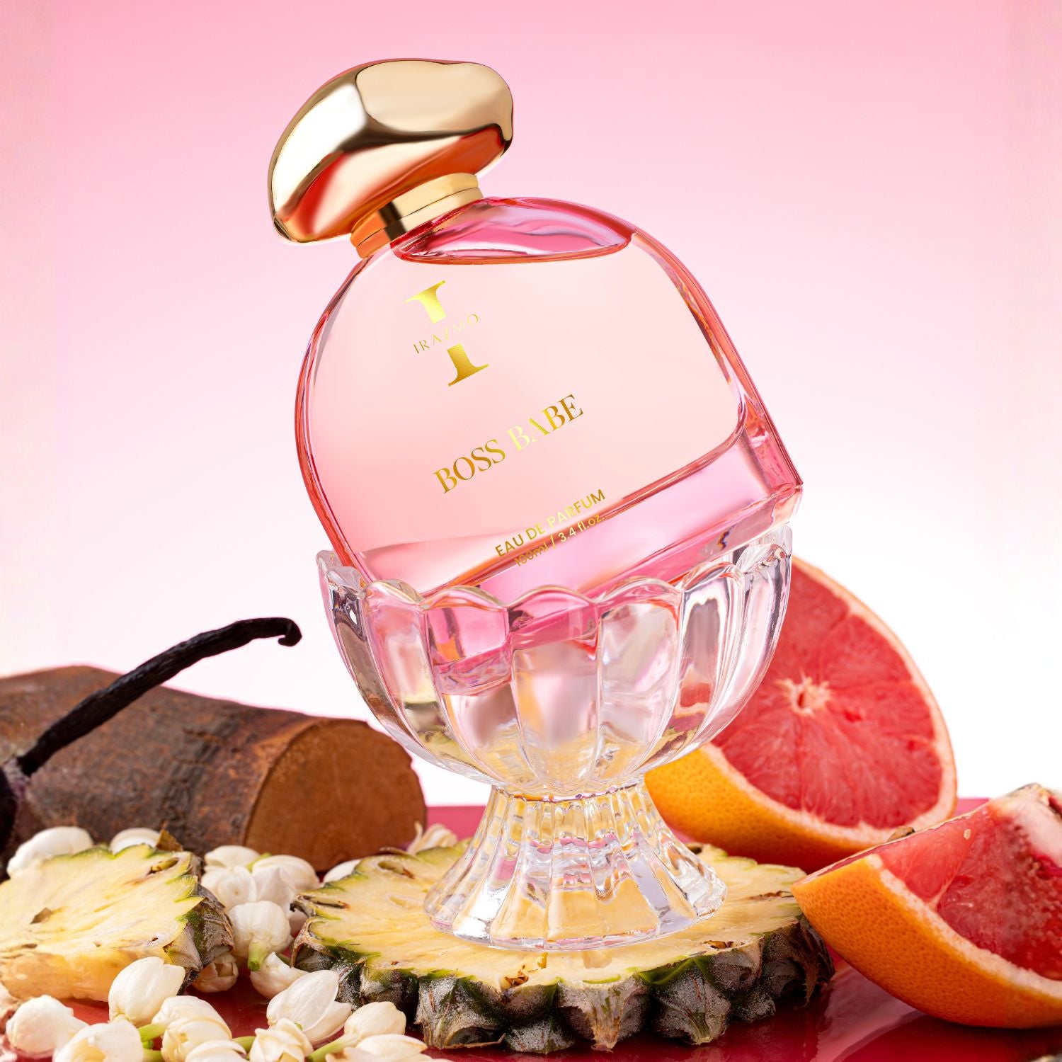 Pink perfume bottle with gold cap on a pink background with fruits and vanilla beans.