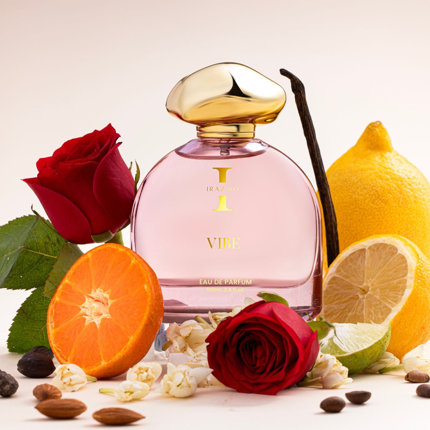 Pink perfume bottle with gold cap surrounded by red roses, lemons, oranges, and vanilla beans on a light background.