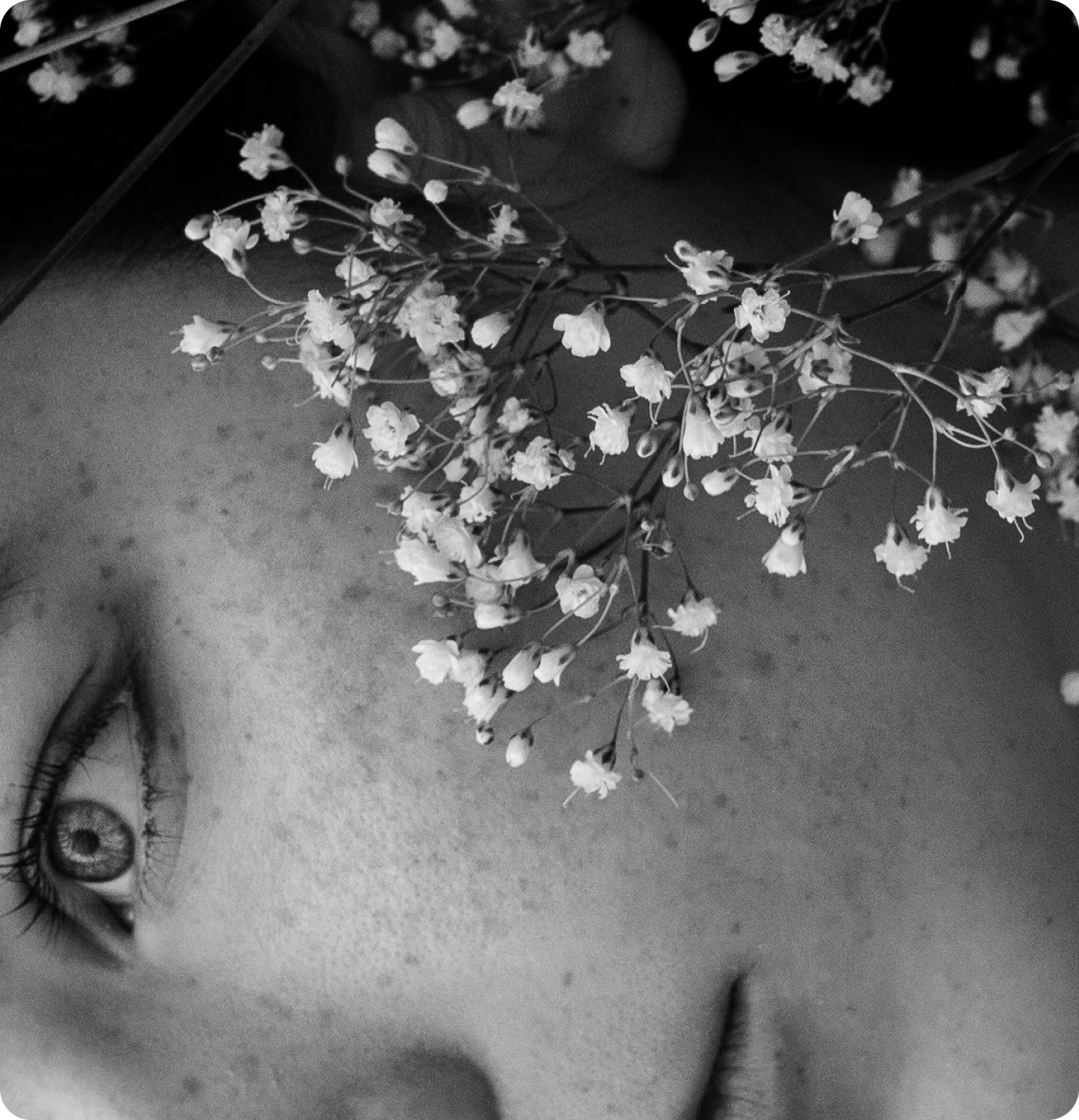 Close-up of a person's face with white flowers on top, black and white photo