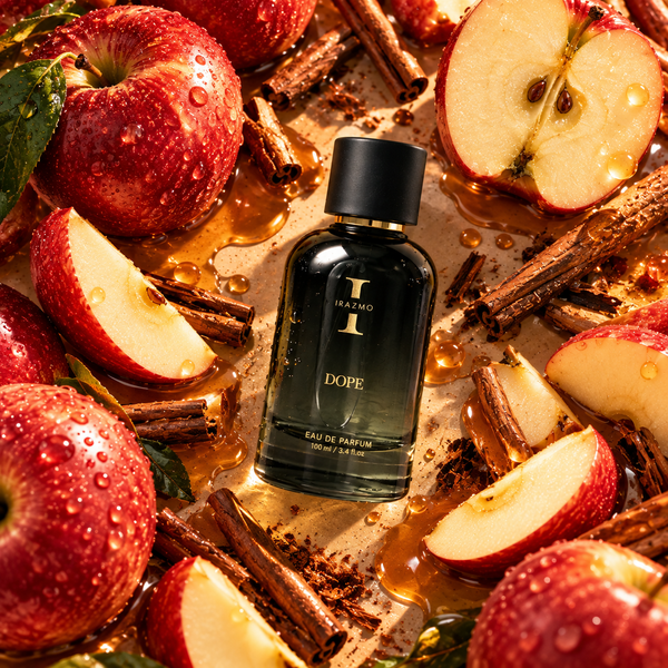 Irazmo Dope 100 ml eau de parfum bottle lying among whole and sliced red apples, cinnamon sticks and golden liquid