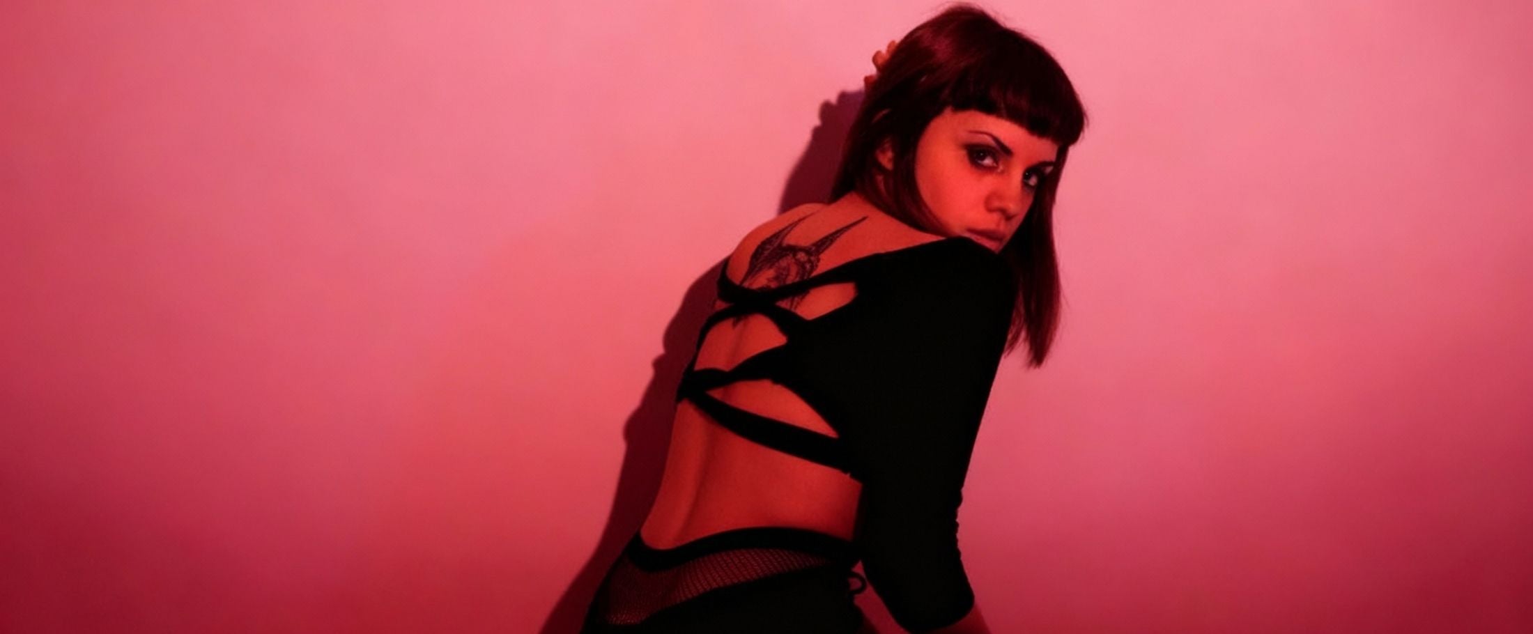 Woman wearing a black outfit with cut-out design against a pink background