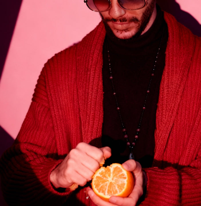 Person in a red sweater holding an orange against a pink background