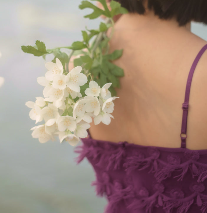 Person wearing a purple dress holding white flowers with a blurred background