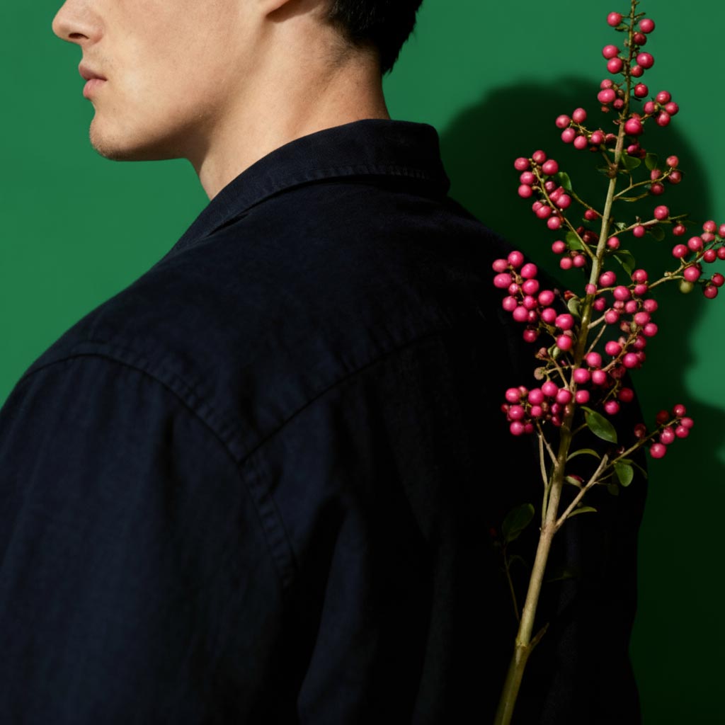 Person wearing a dark shirt holding a branch with pink berries against a green background