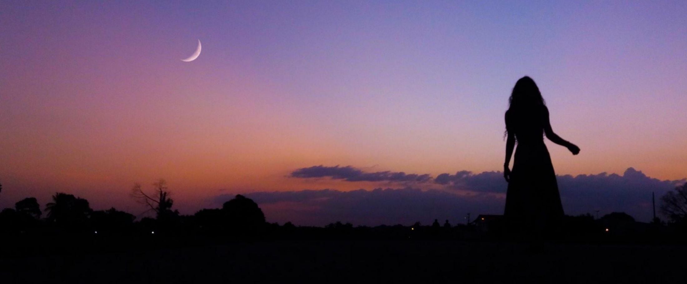Silhouette of a person against a twilight sky with a crescent moon.