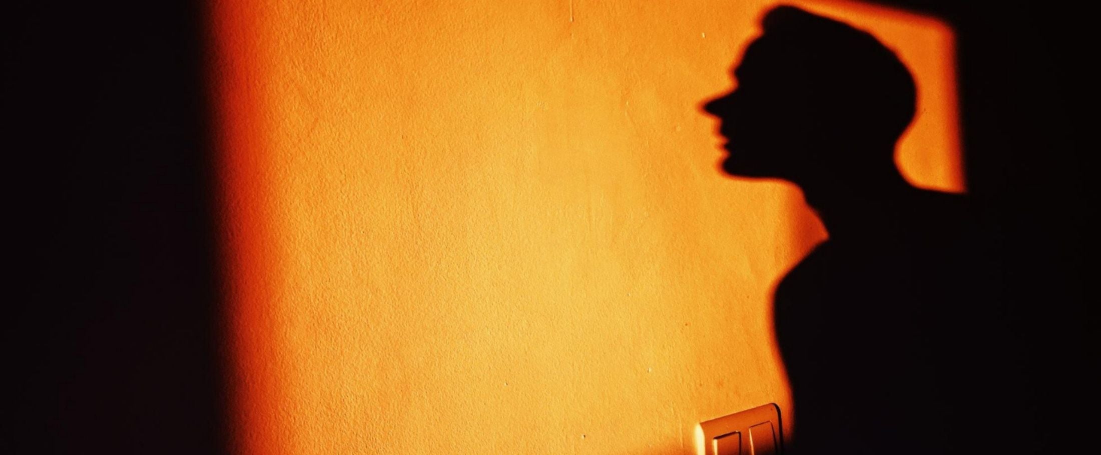 Silhouette of a person against a warm-toned wall.