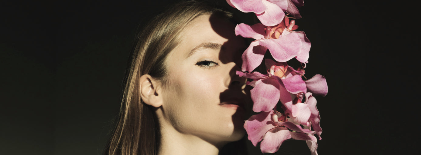 Woman with a floral arrangement covering one side of her face against a dark background