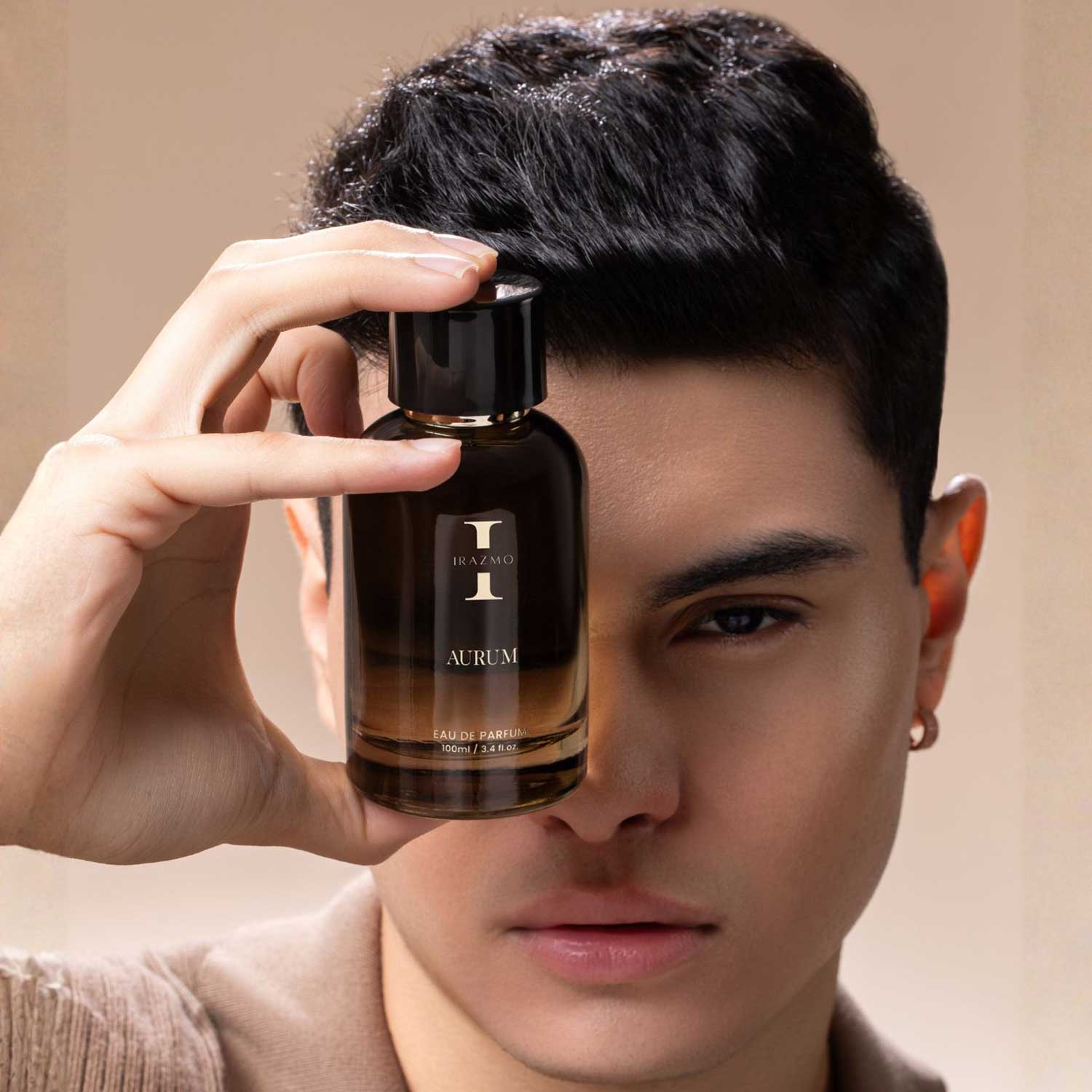 Person holding a perfume bottle labeled 'Aurum' in front of their face against a neutral background