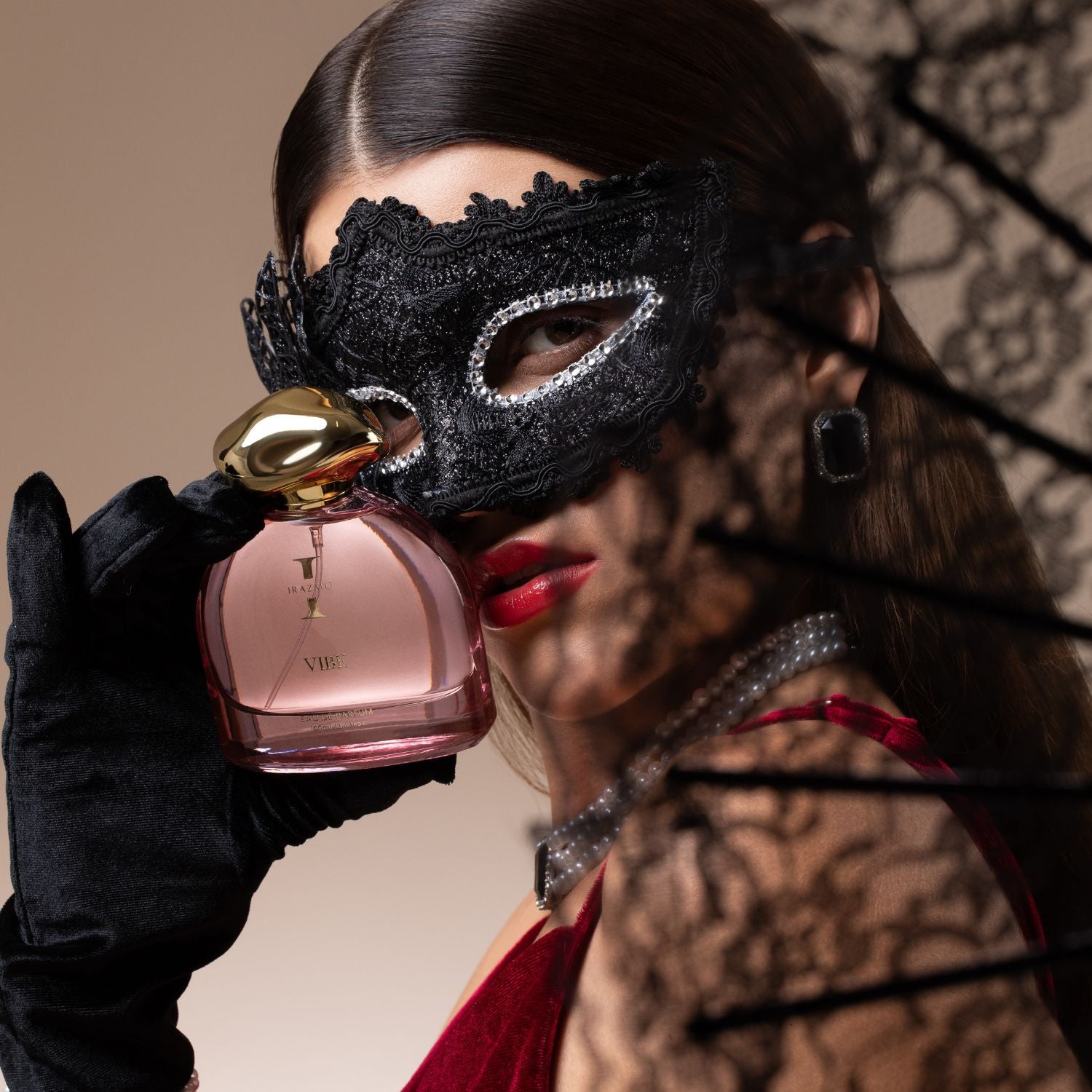 Woman in a black lace mask holding a perfume bottle with a blurred background