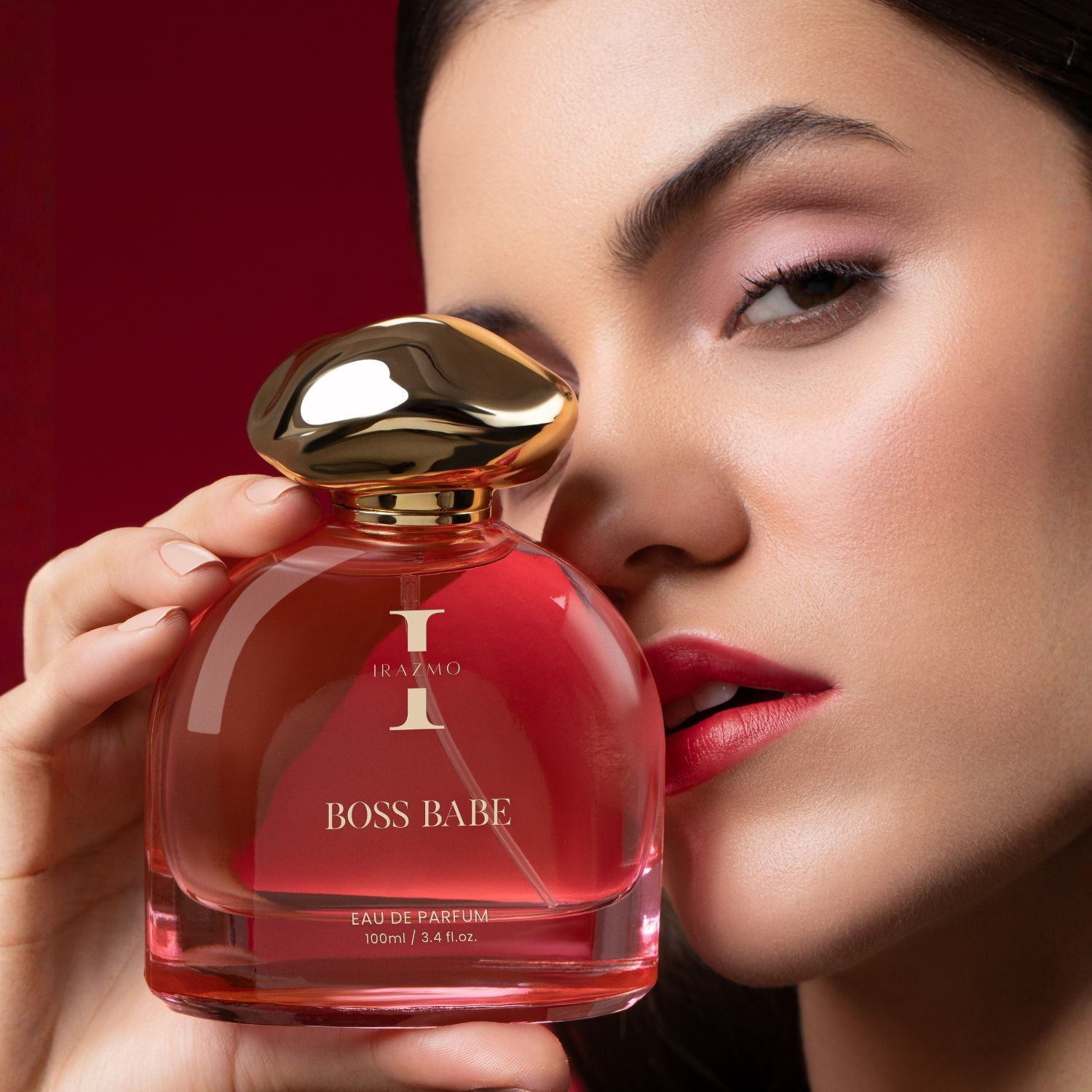 Woman holding a red 'BOSS BABE' perfume bottle with gold cap against a red background