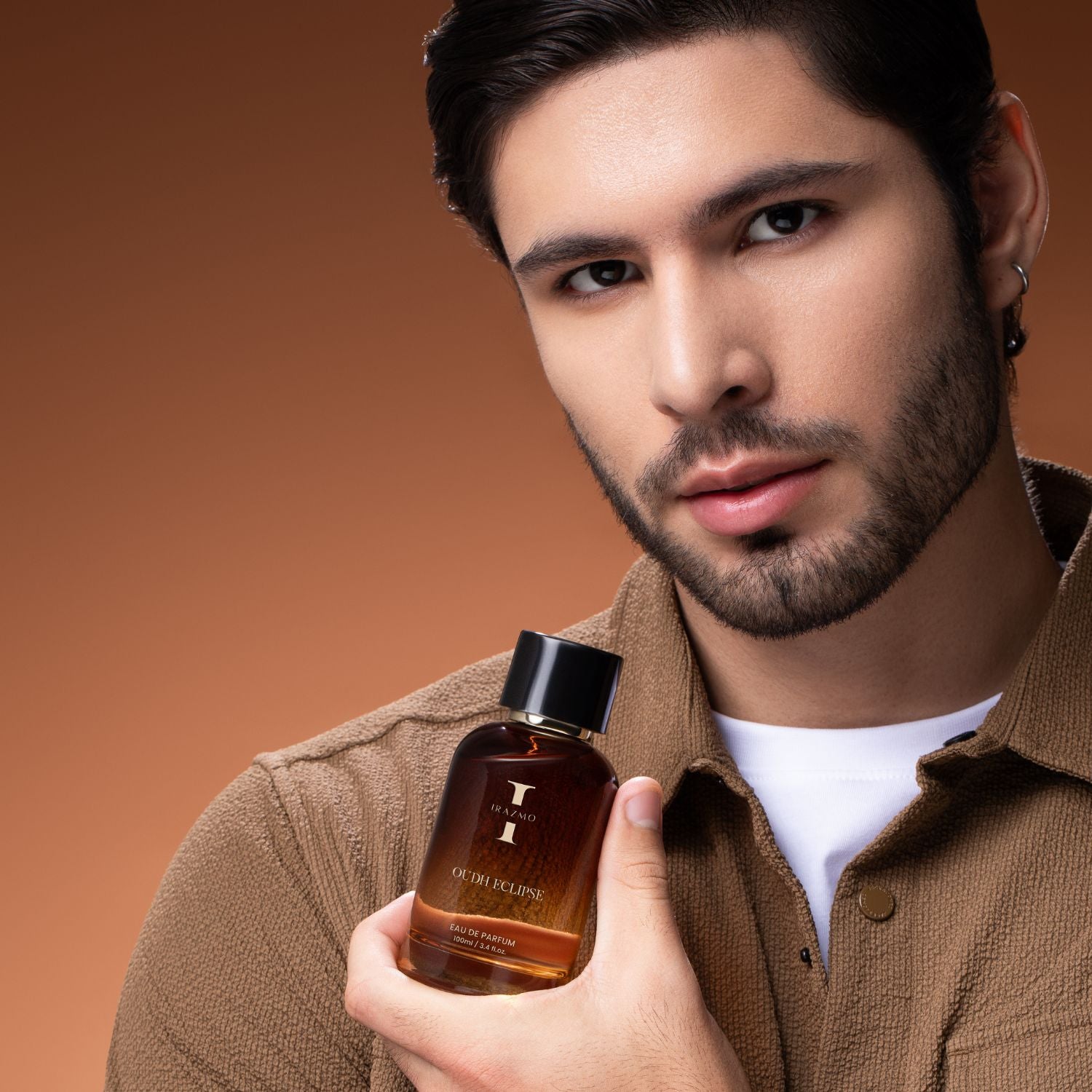 Man holding a bottle of luxury cologne against a brown background