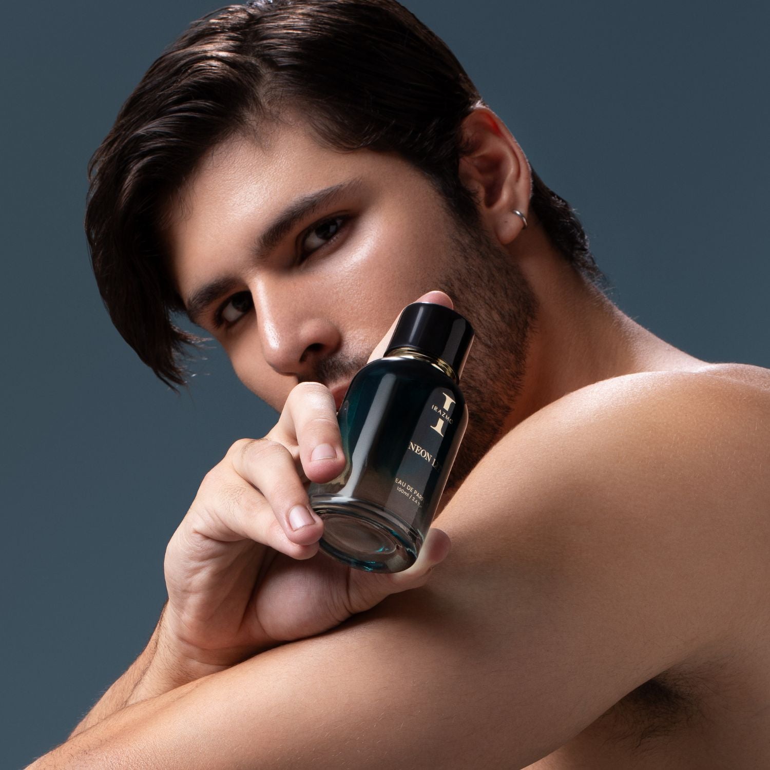 Man holding a perfume bottle against a dark background