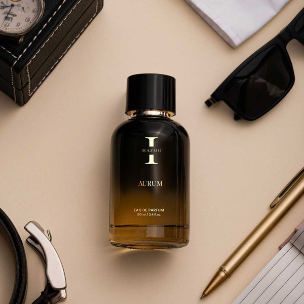 Black perfume bottle labeled 'Iraemo Aurum' on a beige surface with sunglasses, pen, and other items.