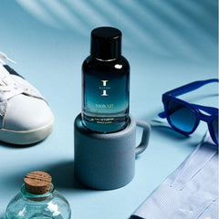 Perfume bottle labeled 'Neon Lit' on a blue surface with a shoe, sunglasses, and other items.