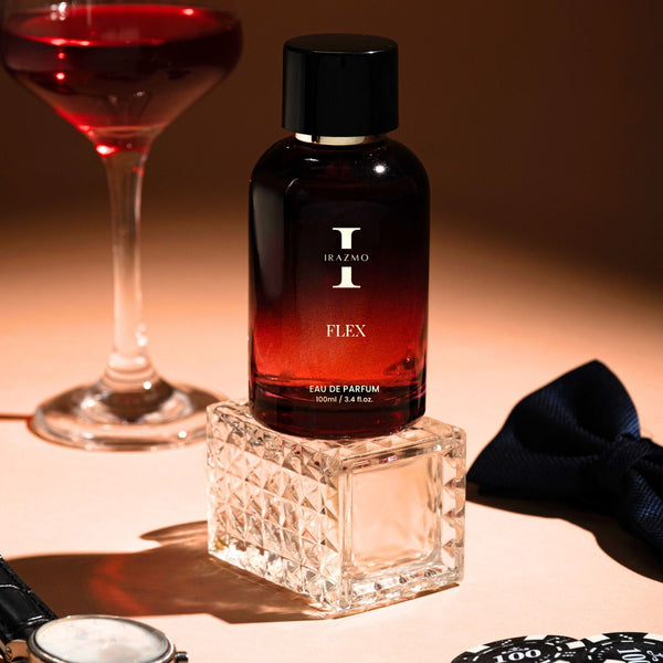Perfume bottle labeled 'Flex' with a glass of red wine, bow tie, and watch on a table.