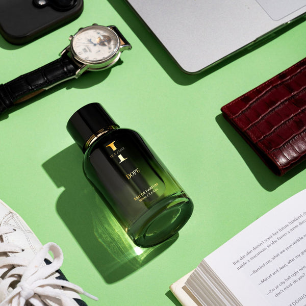 Green perfume bottle on a green surface with a watch, wallet, and other items.