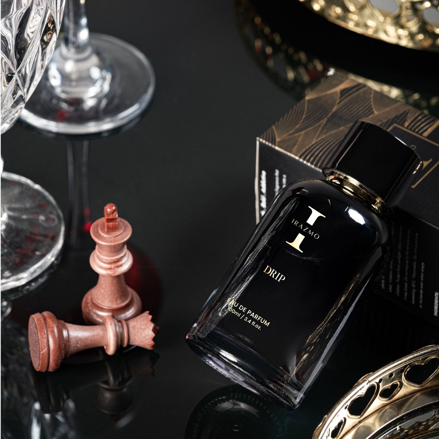 Black perfume bottle labeled 'DRIP' with chess pieces and decorative items on a reflective surface.