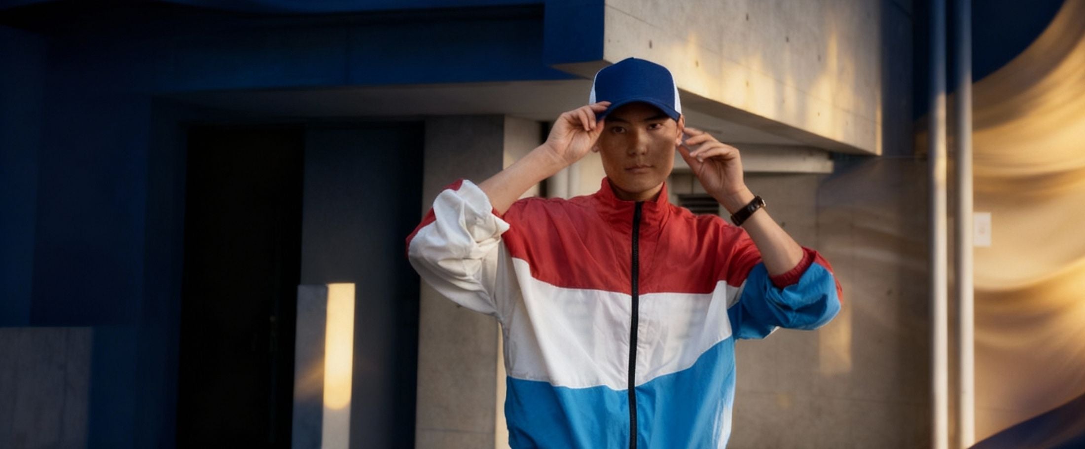 Person wearing a red, white, and blue jacket with a cap in an urban setting
