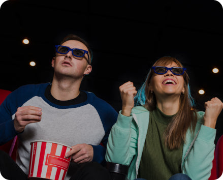 Two people at a movie theater wearing 3D glasses, one holding popcorn.